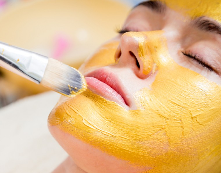 Mulher jovem tendo máscara de ouro aplicada em seu rosto para tratamento estético